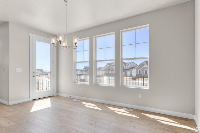 empty room with baseboards, a notable chandelier, visible vents, and wood-type flooring