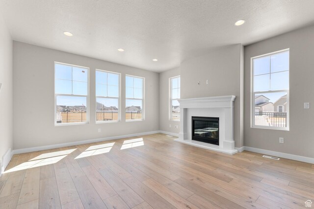 unfurnished living room with a glass covered fireplace, baseboards, light wood finished floors, and visible vents