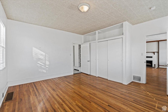 unfurnished bedroom featuring dark wood-type flooring, a closet, and a brick fireplace