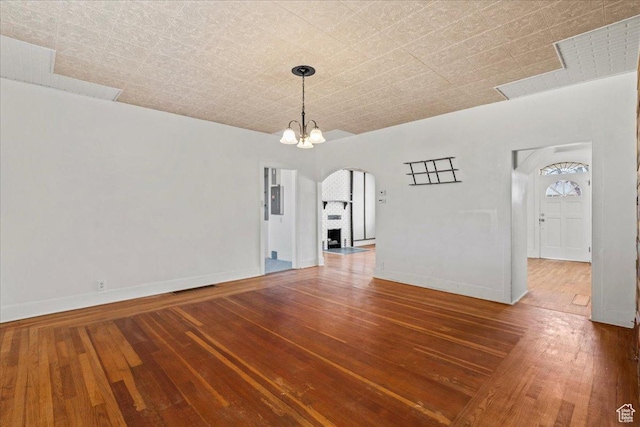 unfurnished dining area with an inviting chandelier, wood-type flooring, a fireplace, and electric panel