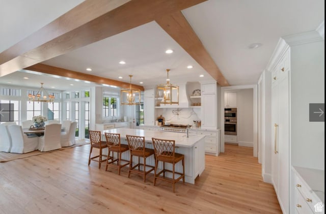 kitchen with beamed ceiling, white cabinetry, pendant lighting, and an inviting chandelier