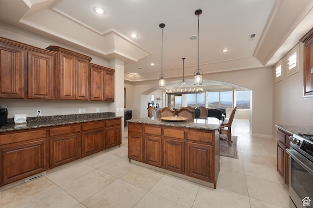 kitchen featuring pendant lighting, stainless steel stove, a tray ceiling, a kitchen island, and dark stone counters