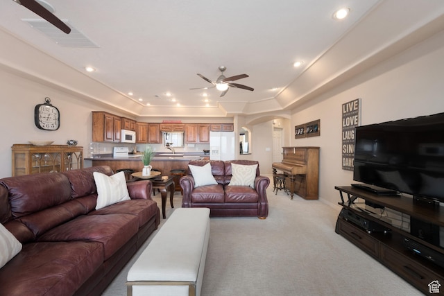 carpeted living room with ceiling fan, a tray ceiling, and sink