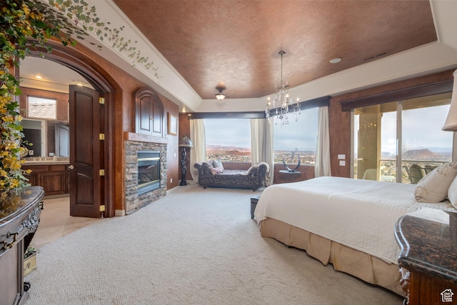 carpeted bedroom featuring ensuite bath, a chandelier, a fireplace, and a tray ceiling