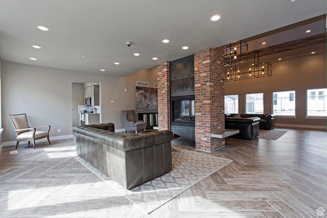living room featuring an inviting chandelier, a textured ceiling, a brick fireplace, and light parquet floors