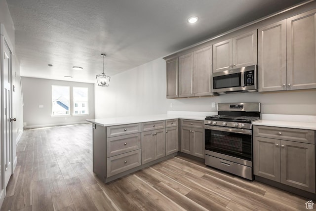 kitchen with appliances with stainless steel finishes, wood-type flooring, a textured ceiling, decorative light fixtures, and kitchen peninsula