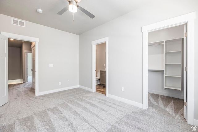 unfurnished bedroom with ensuite bath, a spacious closet, light carpet, a closet, and ceiling fan