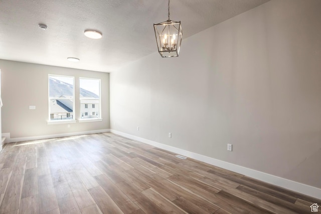 unfurnished room with an inviting chandelier, wood-type flooring, and a textured ceiling