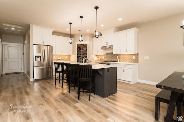 kitchen with stainless steel appliances, a center island with sink, white cabinets, and decorative light fixtures