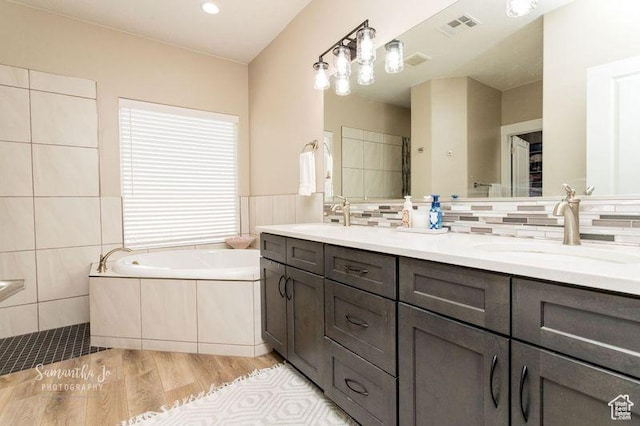 bathroom featuring tile walls, vanity, hardwood / wood-style floors, decorative backsplash, and a washtub