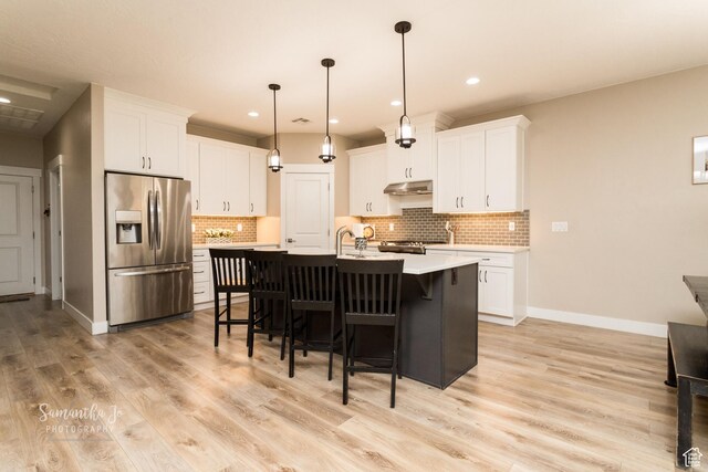 kitchen featuring tasteful backsplash, decorative light fixtures, appliances with stainless steel finishes, an island with sink, and white cabinets