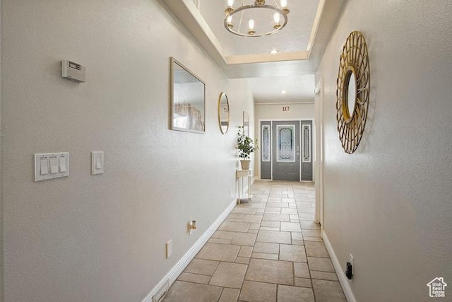 hall featuring a tray ceiling and a chandelier