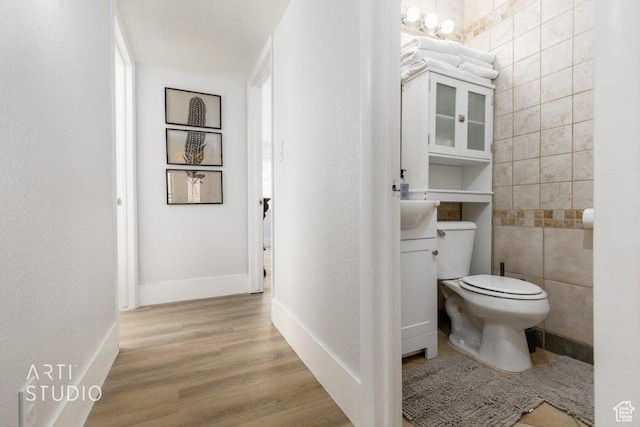 bathroom featuring wood-type flooring, toilet, tile walls, and vanity