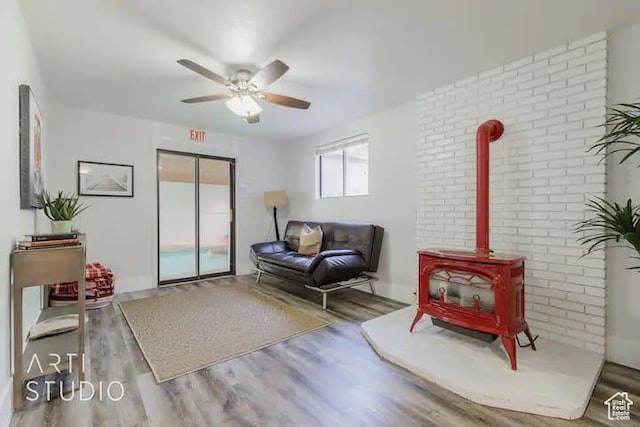 sitting room with hardwood / wood-style flooring, brick wall, ceiling fan, and a wood stove