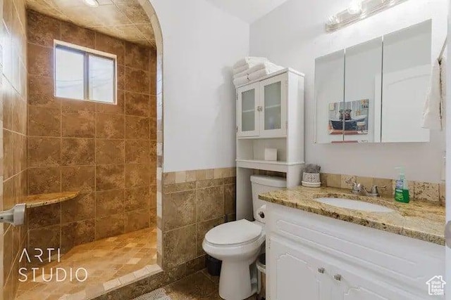 bathroom featuring vanity, a tile shower, tile walls, and toilet