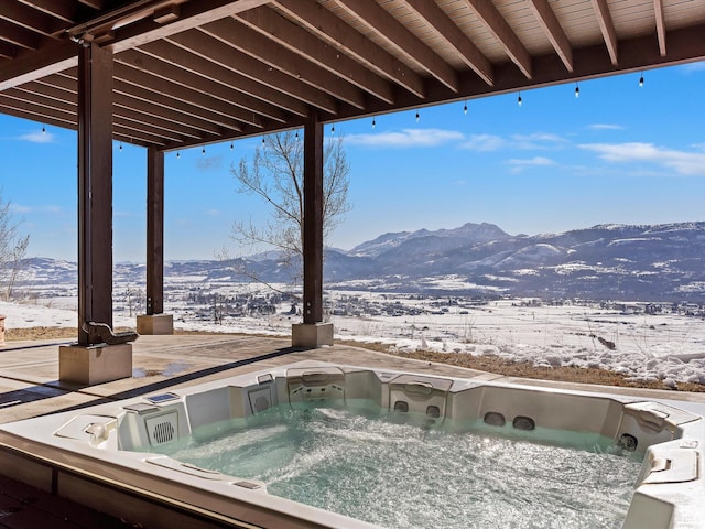snow covered patio featuring a hot tub and a mountain view