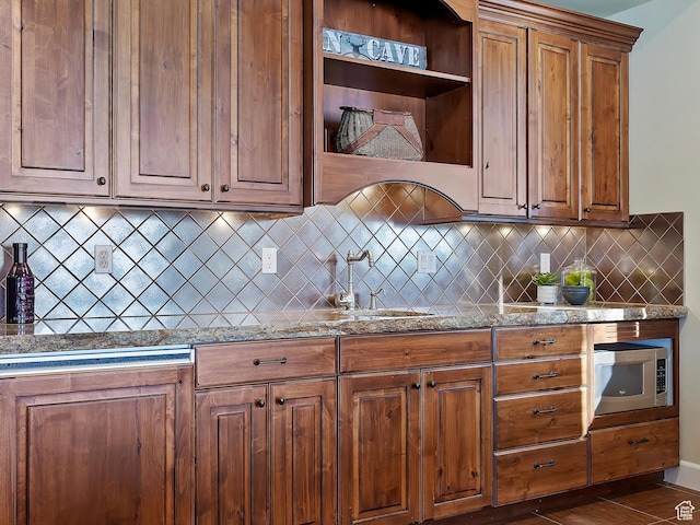 kitchen featuring stainless steel microwave, sink, tasteful backsplash, and light stone countertops
