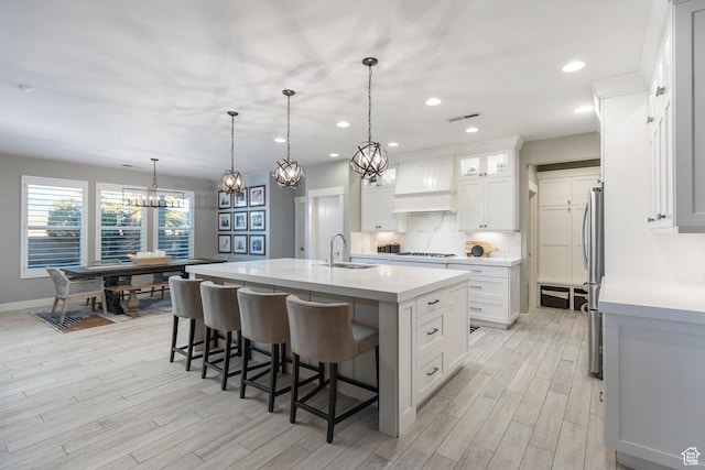 2305 E 3350 S, St George, UT 84790 - kitchen with light wood finished floors, a sink, a kitchen island with sink, tasteful backsplash, and custom exhaust hood