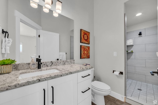 bathroom with hardwood / wood-style flooring, tiled shower, vanity, and toilet