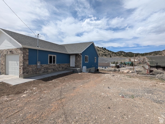 view of home's exterior with a mountain view, driveway, stone siding, and a garage