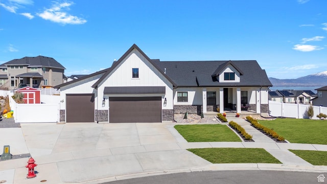 modern farmhouse style home featuring stone siding, fence, a front lawn, driveway, and a mountain view