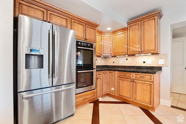 kitchen featuring backsplash, stainless steel appliances, dark stone counters, and light tile patterned flooring