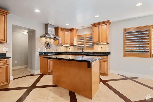 kitchen featuring sink, wall chimney range hood, a kitchen island, dark stone counters, and backsplash
