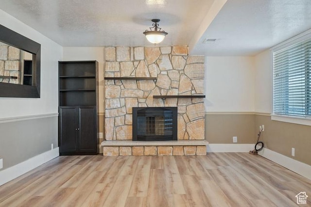 unfurnished living room featuring hardwood / wood-style floors, a stone fireplace, and a textured ceiling