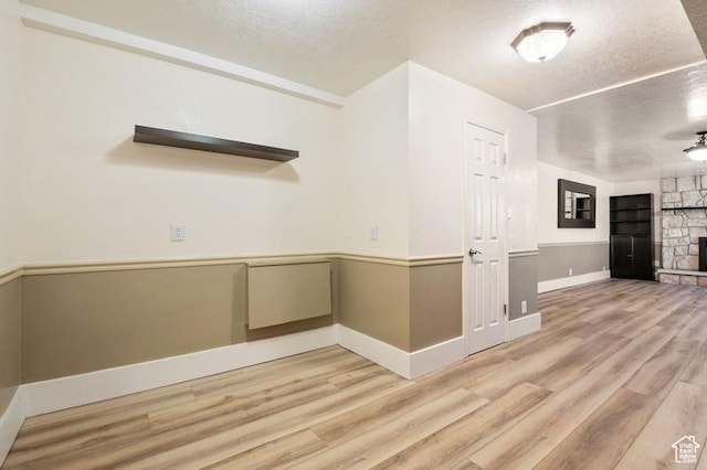 empty room featuring a fireplace, light hardwood / wood-style flooring, and a textured ceiling