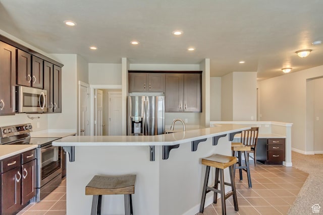 kitchen featuring dark brown cabinetry, a kitchen breakfast bar, appliances with stainless steel finishes, and recessed lighting