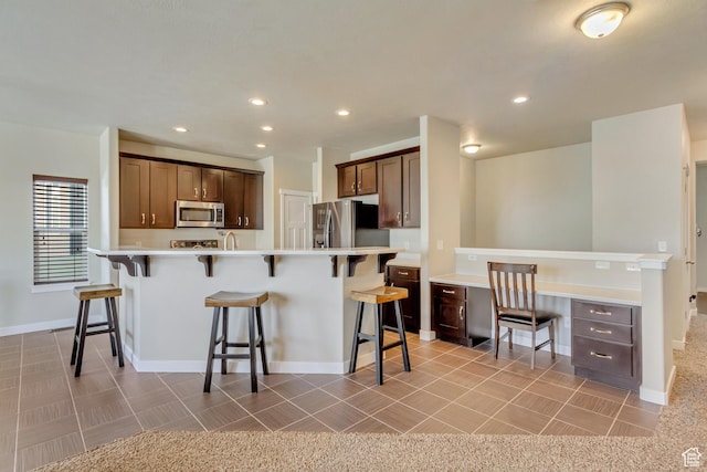 kitchen featuring a sink, light countertops, a kitchen breakfast bar, baseboards, and appliances with stainless steel finishes