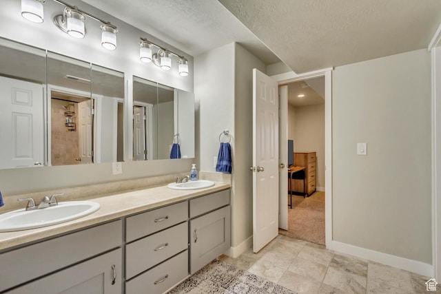 bathroom featuring baseboards, a textured ceiling, double vanity, and a sink