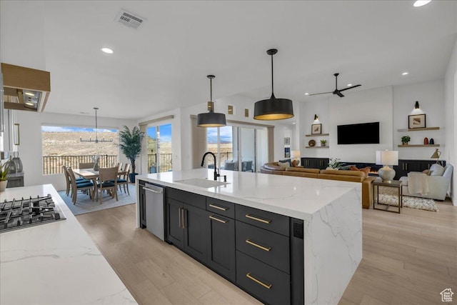 kitchen with pendant lighting, light stone countertops, sink, and a center island with sink