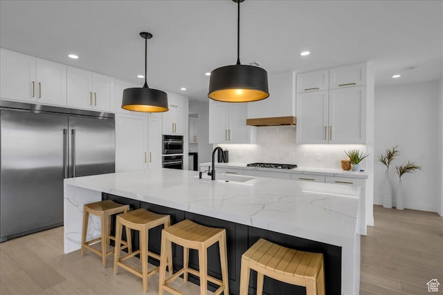 kitchen with built in fridge, an island with sink, sink, and white cabinets