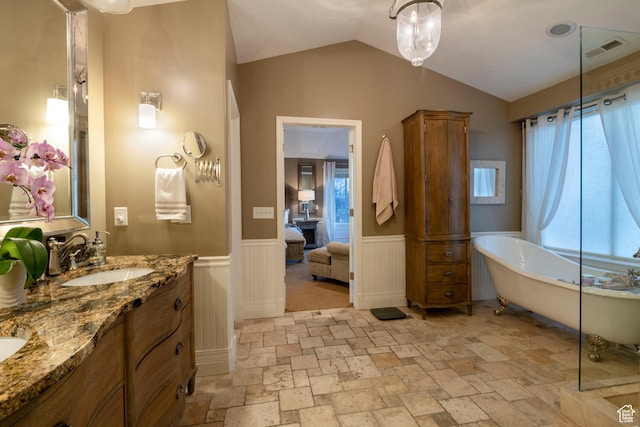 6658 S Caracol Cv, Cottonwood Heights, UT 84121 - ensuite bathroom featuring a soaking tub, stone tile floors, wainscoting, double vanity, and vaulted ceiling