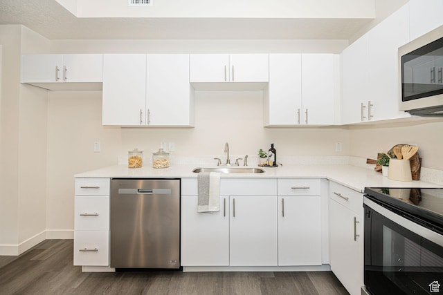 kitchen with light countertops, appliances with stainless steel finishes, dark wood-style floors, white cabinets, and a sink
