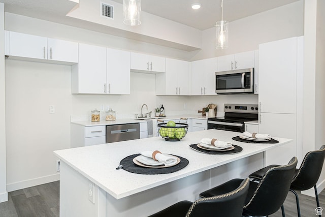 kitchen with visible vents, a breakfast bar, appliances with stainless steel finishes, white cabinetry, and a center island