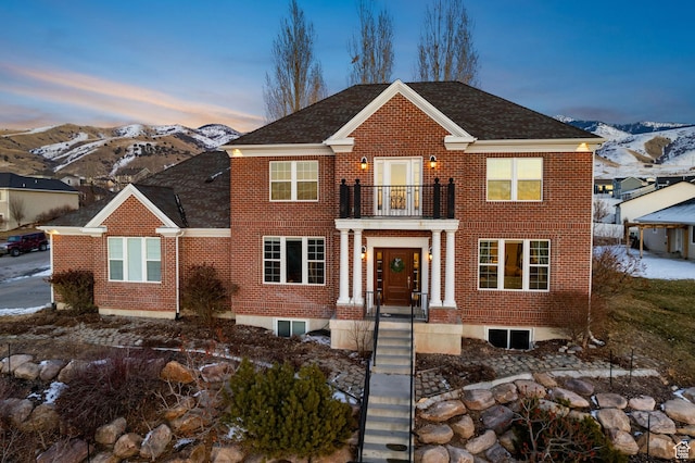 georgian-style home with a balcony, brick siding, a mountain view, and roof with shingles