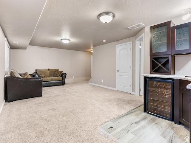 carpeted living room featuring wine cooler, a textured ceiling, and bar