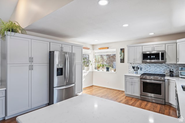 kitchen featuring stainless steel appliances, tasteful backsplash, hardwood / wood-style flooring, and gray cabinetry
