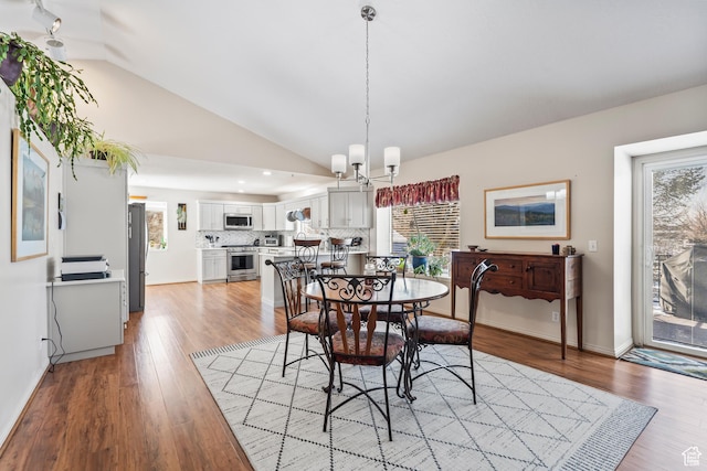 dining area with vaulted ceiling, a notable chandelier, and light hardwood / wood-style floors