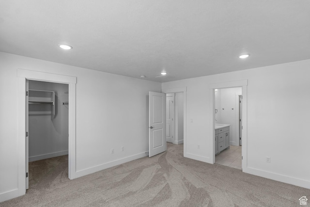 unfurnished bedroom with light carpet, a spacious closet, a closet, and ensuite bathroom