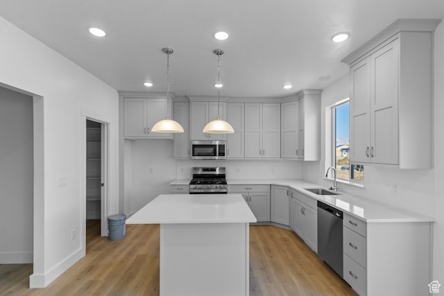 kitchen featuring appliances with stainless steel finishes, decorative light fixtures, sink, a center island, and light hardwood / wood-style floors