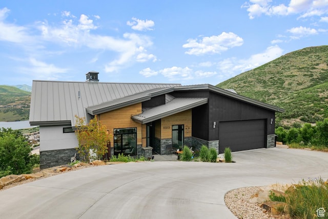 view of front of home featuring a standing seam roof, stone siding, curved driveway, metal roof, and a garage