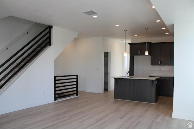 kitchen featuring light hardwood / wood-style flooring, a kitchen island with sink, hanging light fixtures, dark brown cabinetry, and decorative backsplash