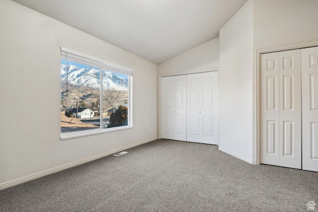 unfurnished bedroom featuring lofted ceiling, carpet floors, and multiple closets