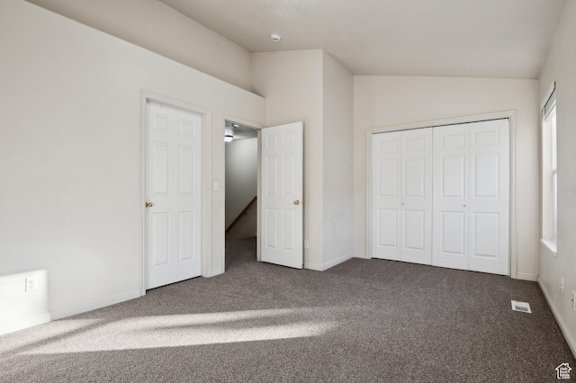 unfurnished bedroom featuring dark colored carpet, vaulted ceiling, and a closet