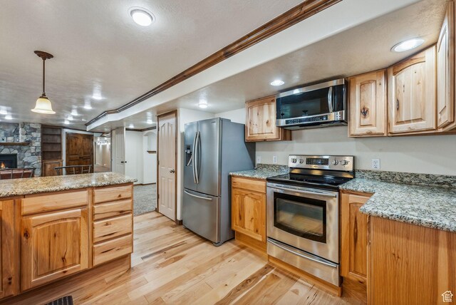 12159 S Swensen Cir, Riverton, UT 84096 - kitchen featuring appliances with stainless steel finishes, light wood-type flooring, a fireplace, decorative light fixtures, and light stone countertops