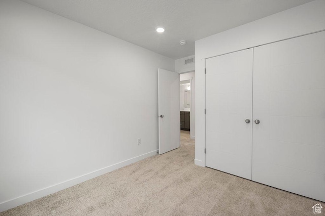 unfurnished bedroom featuring light carpet, baseboards, recessed lighting, and a closet