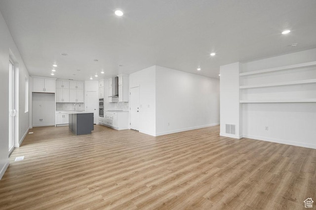 unfurnished living room featuring a sink, recessed lighting, light wood finished floors, and baseboards